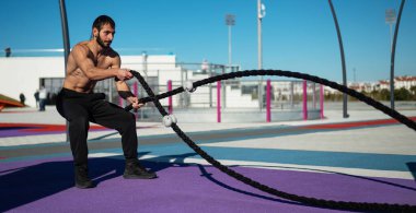 Gömleksiz adam dışarıda halatla egzersiz yapıyor.