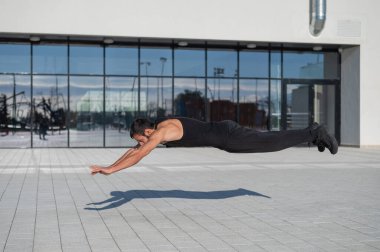 Siyah spor kıyafetli bir adam dışarıda şınav çekerken zıplıyor.