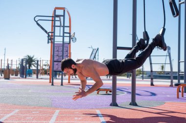 Tişörtsüz adam dışarıda ilmek egzersizi yapıyor.