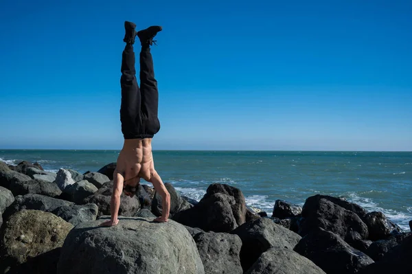 Tişörtsüz Bir Adam Deniz Kenarındaki Kayalarda Amuda Kalkıyor — Stok fotoğraf