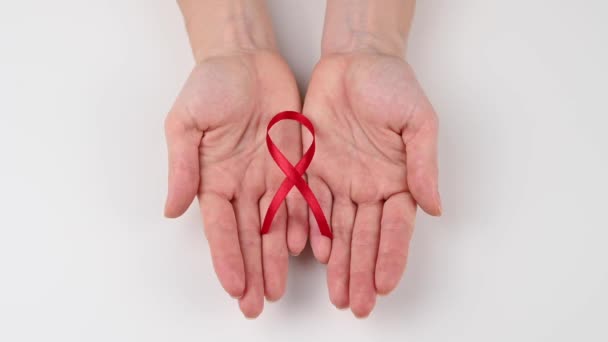 女性が手を開き 白い背景に赤いリボンを示しています エイズとの闘いの象徴 — ストック動画