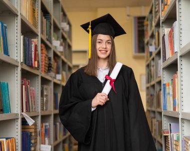Mezuniyet elbisesi içinde, elinde diploması olan mutlu genç bir kadın.