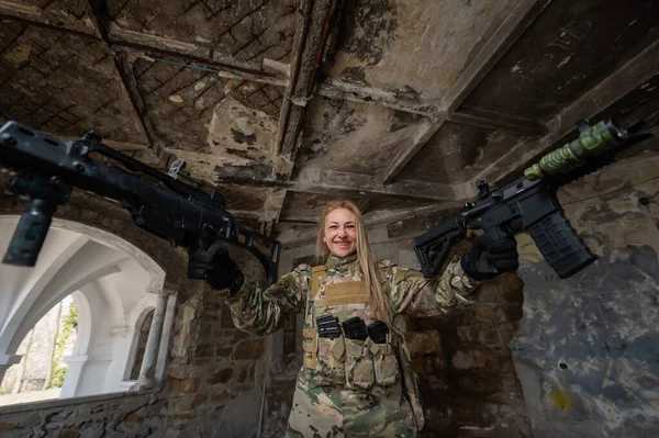 Caucasian woman in army uniform holding two machine guns