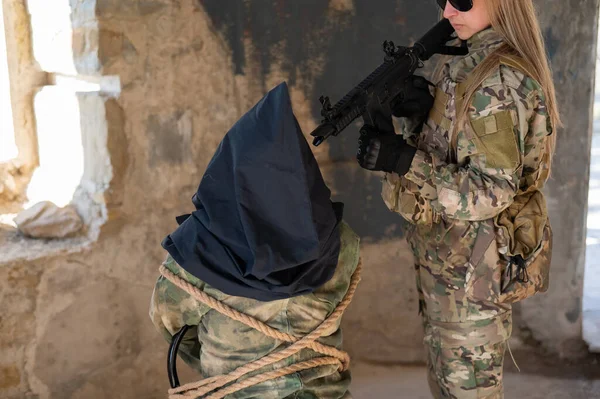 Biała Kobieta Mundurze Wojskowym Trzyma Zakładnika Torbą Głowie Widoku Karabinu — Zdjęcie stockowe