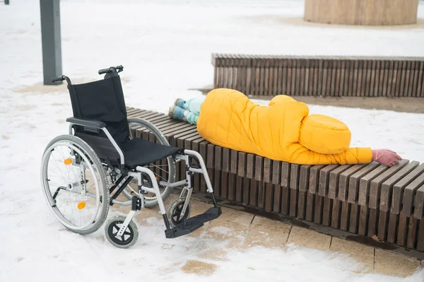 无家可归的女人睡在轮椅旁边的公园长椅上 — 图库照片