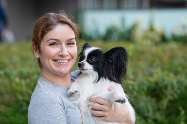 Beyaz, kızıl saçlı bir kadın, pappilion köpeğini açık havada tutuyor. Siyah ve beyaz kıtasal spanyel.