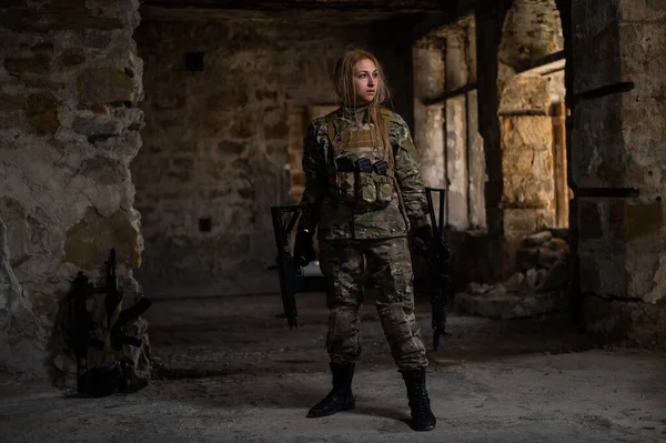 Blonde woman in army uniform holding a firearm in an abandoned building