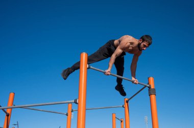 Çıplak gövdeli bir adam yatay çubukta denge sağlar.