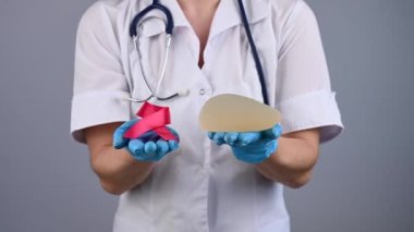 Dr. Mammolog silikon bir göğüs implantı tutuyor ve elini pembe bir kurdeleyle uzatıyor.