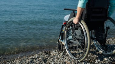 Deniz kıyısında tekerlekli sandalyedeki beyaz kadın. Kadın ellerine yakın çekim