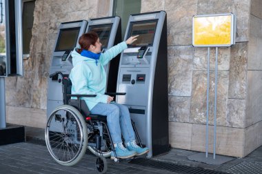 Tekerlekli sandalyedeki beyaz kadın self-servis kasasından tren bileti alıyor.