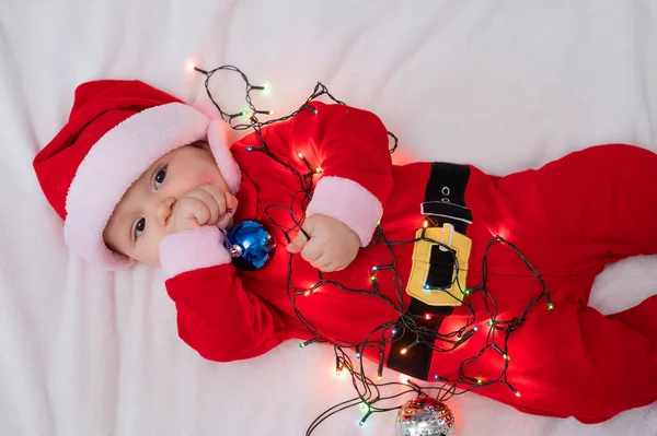 Chłopiec Ubrany Strój Mikołaja Leży Łóżku Bawi Się Świąteczną Girlandą — Zdjęcie stockowe
