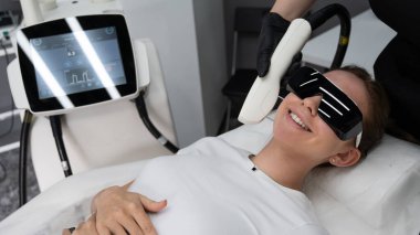 Gözlüklü genç beyaz kadın, fotojenizasyon prosedürü uyguluyor. Güzellik kliniğindeki bir kızın portresi.