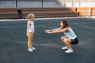 Anne ve kızı spor için dışarı çıkıyorlar. Beyaz kadın ve küçük kız stadyumda spor yapıyorlar.