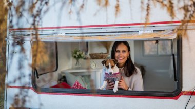 Beyaz kadın köpeği Jack Russell Terrier 'a sarılırken minibüsün camından dışarı bakar. Sonbaharda bir karavanla seyahat et.