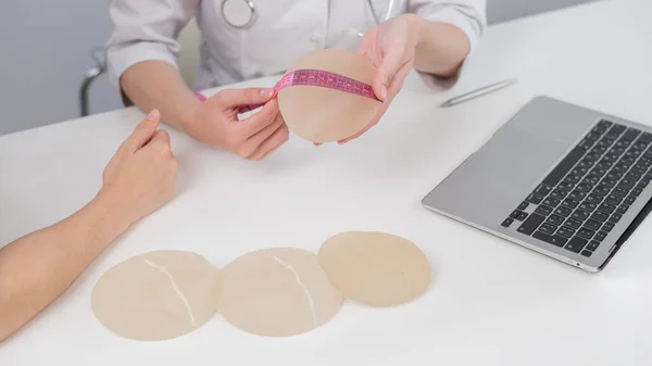 整形外科医は センチメートルテープで乳房インプラントを測定し 女性患者に示す — ストック写真