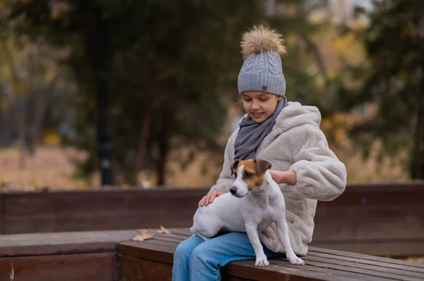 白人の女の子は犬とベンチに座っていますジャック ラッセル テリア秋の公園を散歩 — ストック写真