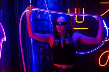 Güneş gözlüklü beyaz kadın neon stüdyoda poz veriyor.