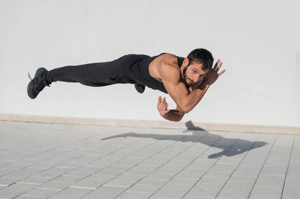 A man in black sportswear jumps while doing push-ups outdoors