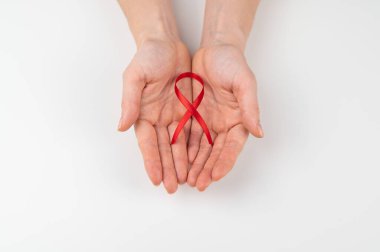 Beyaz arka planda kırmızı kurdeleli bir kadın eli. AIDS 'le mücadelenin sembolü
