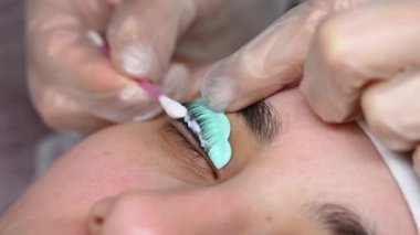 Usta, müşterilerin kirpiklerindeki katman bileşimini pamuklu bezle temizliyor. Kirpik perma prosedürü