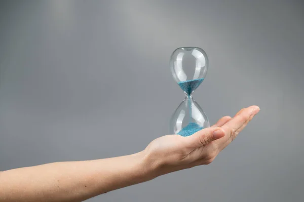 Stock image Woman holding an hourglass on a gray background. Close-up. Copy space