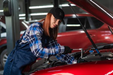 Tulumlu bir kadın tamirci araba tamir ediyor.