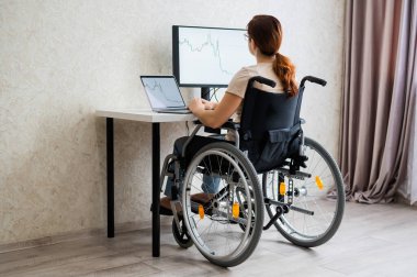 Tekerlekli sandalyedeki beyaz kadın evden bilgisayarla yazı yazıyor. Engelliler için uzak çalışma