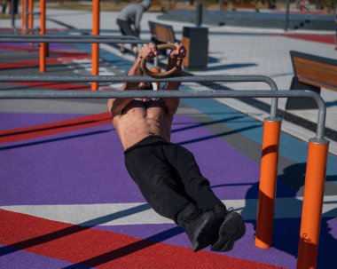 Spor sahasındaki paralel çubuklarda üstsüz adam yatay denge yapıyor.