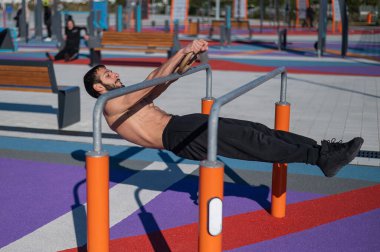 Spor sahasındaki paralel çubuklarda üstsüz adam yatay denge yapıyor.