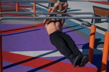 Spor sahasındaki paralel çubuklarda üstsüz adam yatay denge yapıyor.