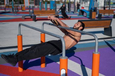 Spor sahasındaki paralel çubuklarda üstsüz adam yatay denge yapıyor.