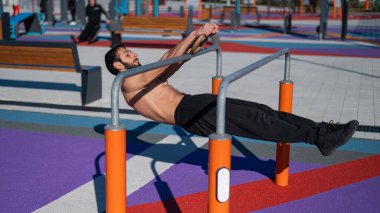 Spor sahasındaki paralel çubuklarda üstsüz adam yatay denge yapıyor.