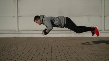 Kapüşonlu bir adam dışarıda şınav çekerken zıplıyor.