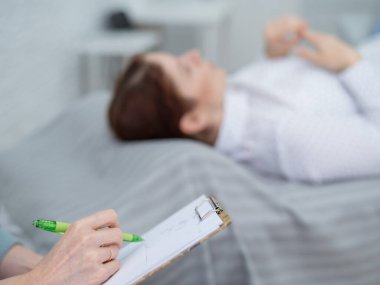 Kafkasyalı bir kadın kanepeye uzanıp duygularını ifade ederken, bir psikolog tablete notlar alır.