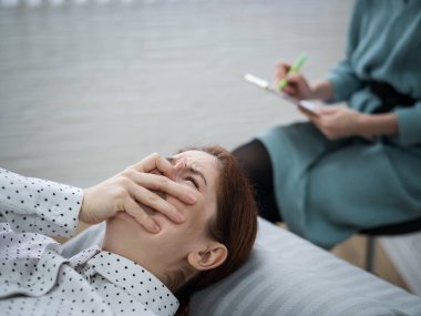 Psikologla bir seansta kanepede yatarken ağlayan beyaz bir kadın.