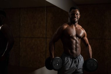 Kas yığını koyu tenli adam dambıllarla egzersiz yapıyor.