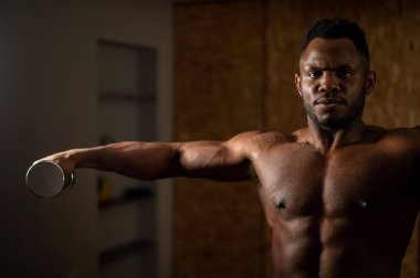 Çekici Afrikalı Amerikalı adam dambıllarla kol egzersizi yapıyor.