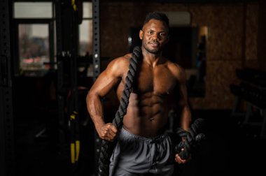 Kaslı Afrikalı Amerikalı adam spor salonunda iple poz veriyor.