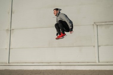 Kapüşonlu beyaz adam elleri dışarıda dizlerinin üzerinde yükseğe zıplıyor.