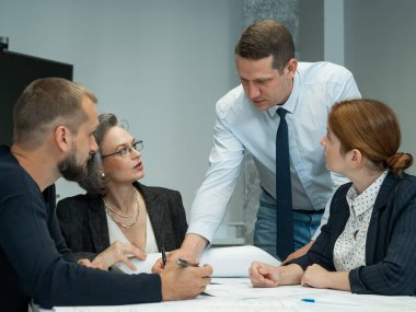 Patron ofis konferans odasında üç çalışana talimat verir. Beyin fırtınası yapan mühendisler ve mimarlar.