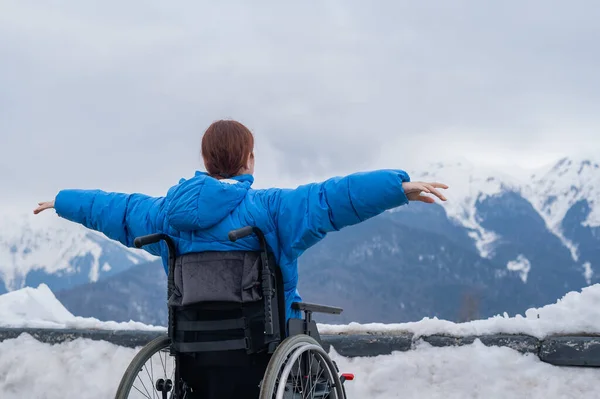 Rear view of a woman in a wheelchair spread her arms to the side like wings in the mountains in winter