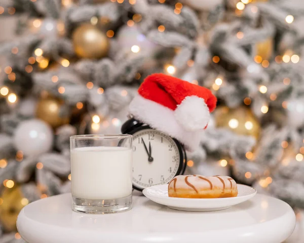 Будильник Шляпе Санта Клауса Стаканом Молока Пончиком Фоне Рождественской Елки — стоковое фото