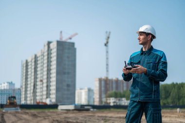 Kasklı ve tulumlu bir adam inşaat alanındaki bir dronu kontrol ediyor. İnşaatçı teknik bir hata yapıyor.