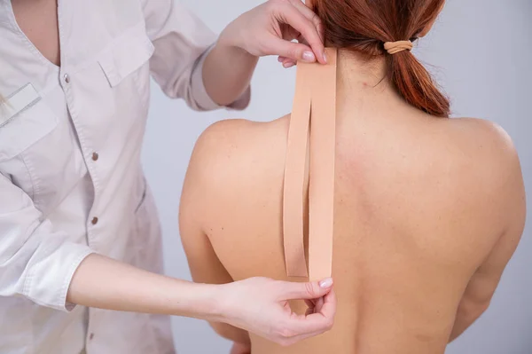 Female doctor glues kinesio tapes on the patients shoulder