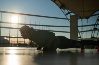 Genç beyaz adam gün batımında boks ringinde şınav çekiyor.