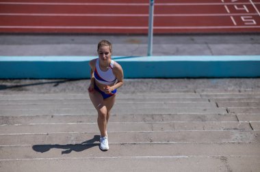 Genç beyaz kadın stadyum merdivenlerinde koşuyor.