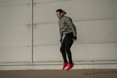 Kapüşonlu beyaz adam elleri dışarıda dizlerinin üzerinde yükseğe zıplıyor.