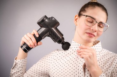 Beyaz bir kadın sırt ve omuzlarında ağrı için masaj tabancası kullanıyor.