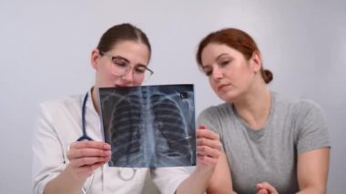 Doktor beyaz bir kadına danışıyor ve akciğerlerin röntgenleri hakkında yorum yapıyor.